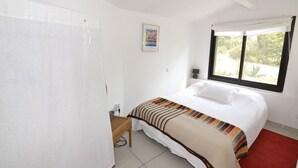 Une chambre à coucher avec un lit, une fenêtre avec des rideaux, une lampe fixée au mur et une petite table avec une chaise.