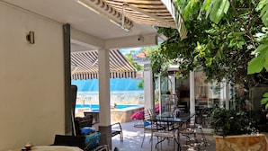 Un'area patio esterna con piscina, posti a sedere coperti e un fioriere in pietra.