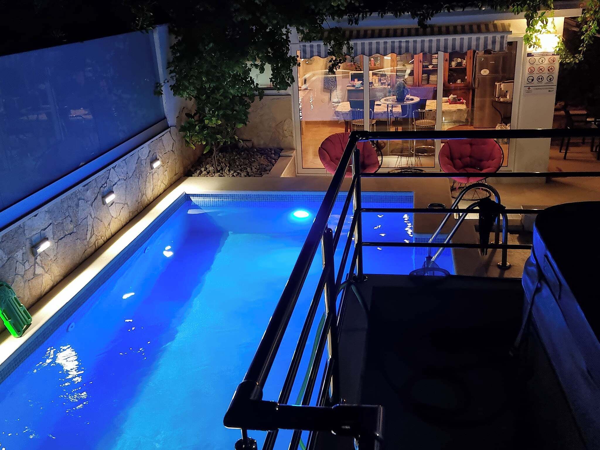 A swimming pool with a metal ladder, surrounded by a stone wall and a small garden area.