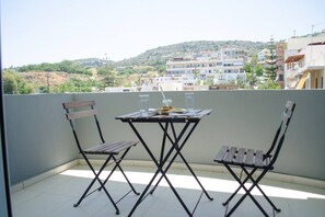 A balcony with a table and two chairs, overlooking a residential area with buildings and hills.