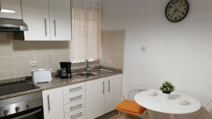 Una cocina con estufa, tostadora, fregadero y un reloj en la pared.