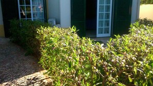 Een gebouw met twee open ramen en groene luiken, omgeven door begroeiing.