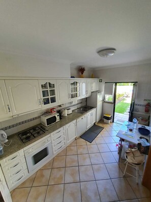 A kitchen with white cabinets, a gas stove, a microwave, and a sink. There is a small rug on the floor and a table with a water bottle and a bowl.