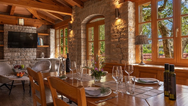 A dining area with a stone wall, wooden beams, and large windows overlooking greenery. - Quiet and Cozy Cottage in Nature (Buje)