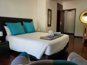 Un lit bien fait, avec une literie blanche et deux coussins turquoise, une petite table de chevet avec une lampe et un plancher en bois.
