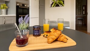 A breakfast setting with a croissant, jam, honey, and orange juice on a wooden board.