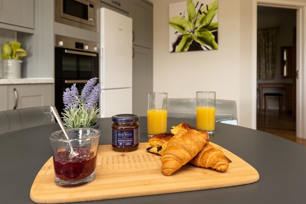 En morgenmadsopstilling med croissant, marmelade, honning og appelsinjuice på en træplade.