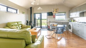 A modern kitchen with a dining area, featuring a green leather sofa, a dining table with chairs, and a view of the outdoors.