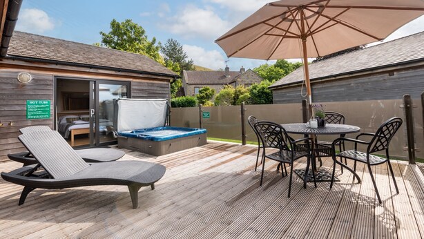 A wooden deck with lounge chairs, a hot tub, and a table with chairs.