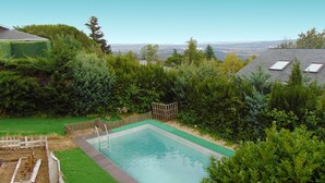 A rectangular swimming pool surrounded by a wooden deck and lush greenery.