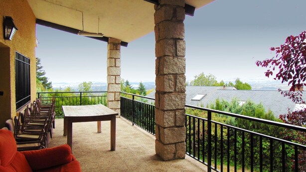 A balcony with stone pillars, a table, and chairs.