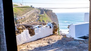 A stone patio with a view of the ocean and a white wall. - Azenhas Beach Room - Azehas do Mar (Lisboa)