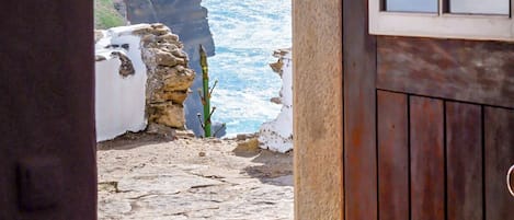 A stone pathway leading to a coastal view with a wooden door and window.