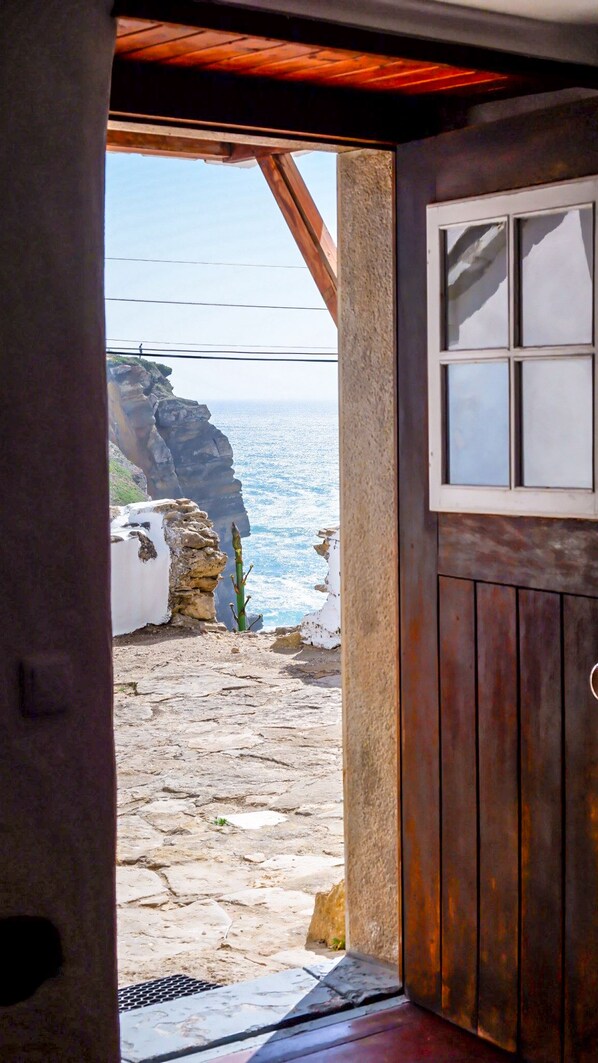 A stone pathway leading to a coastal view with a wooden door and window.