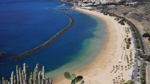 A coastal landscape with a beach, cacti, and a distant town. - Luxury Bungalow Costa Adeje; Heated Pool, Air Conditioner, WiFi & Parking free (Adeje)