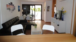 A modern living room with a dark brown sofa, white chairs, a small table, and a TV on a white cabinet. - Luxury Bungalow Costa Adeje; Heated Pool, Air Conditioner, WiFi & Parking free (Adeje)