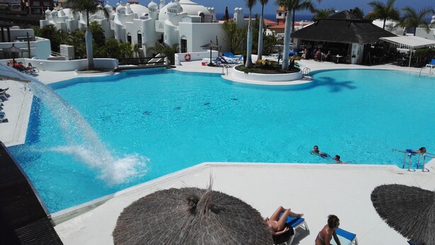 A large swimming pool with clear blue water, surrounded by white buildings and palm trees. - Luxury Bungalow Costa Adeje; Heated Pool, Air Conditioner, WiFi & Parking free (Adeje)