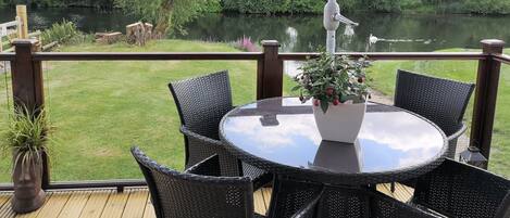 Une terrasse dotée d’une table ronde et de quatre chaises, offrant une vue sur une rivière et la verdure environnante.