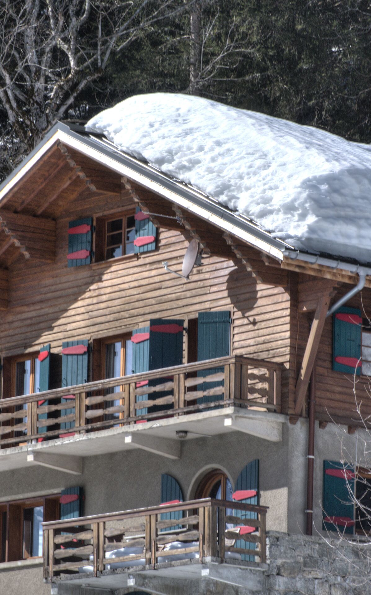 Un chalet en bois doté d’un balcon, d’un toit enneigé et de nombreuses fenêtres équipées de volets.