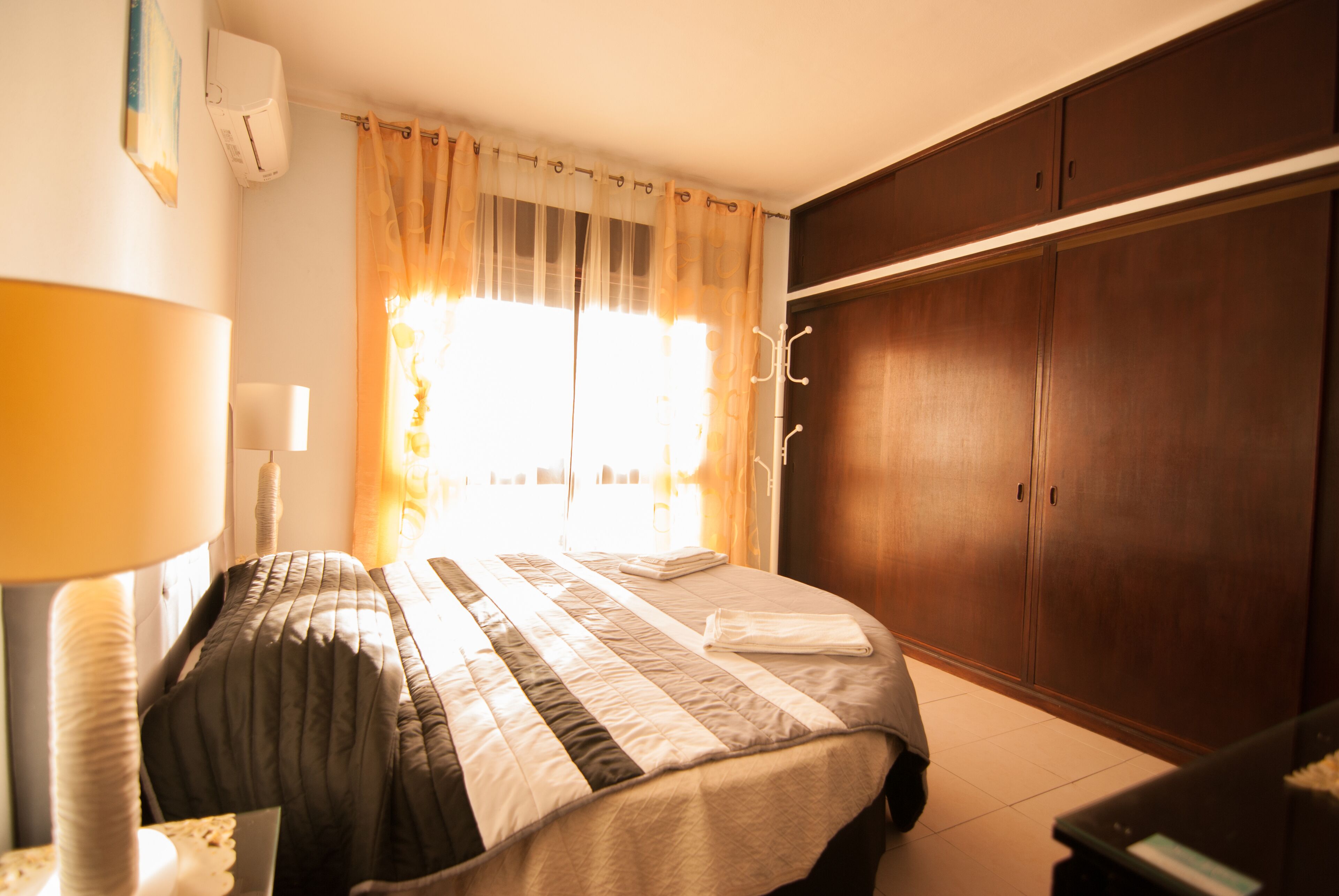 Ein Schlafzimmer mit Bett, Vorhängen, einem Kleiderschrank und einer Lampe.
