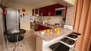 Eine kompakte Küche mit Kühlschrank, Mikrowelle und Kaffeemaschine. Es gibt drei Barhocker und einen kleinen Tisch mit einer Glaskuppel.