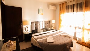 Ein Hotelzimmer mit einem großen Bett, zwei Nachttischen mit Lampen, einer dunklen Holztür und einem Fenster mit Vorhängen.