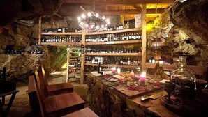 Een bar met houten planken vol flessen, een houten toonbank met kaarsen en een rustieke stenen muur.