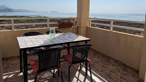 Une terrasse avec une table et des chaises, un pot de fleurs et une vue sur la mer et les montagnes.