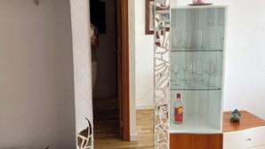 Une pièce avec un plancher en bois, un mur blanc, une bibliothèque remplie de livres, une vitrine contenant des verres à vin et un banc.