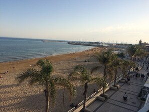 Ein Strand mit Palmen, einer Uferpromenade und Blick aufs Meer.