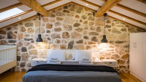A bedroom with a stone wall, wooden beams, a bed with white bedding, and a crib. - Villa Miandri with heated pool (Debeljak)