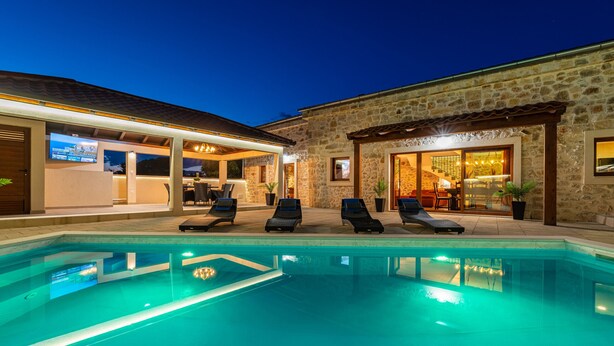 A swimming pool with lounge chairs, a stone building with a covered patio, and a well-lit interior. - Villa Miandri with heated pool (Debeljak)