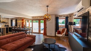 A modern living room with a sofa, a round table, and a TV. There is a kitchen area with a dining table and chairs. - Villa Miandri with heated pool (Debeljak)