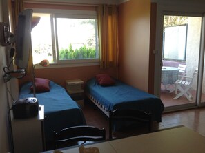 A room with two single beds, a desk with a computer, a chair, and a window with curtains. - Charming studio with sea view (Hyères)