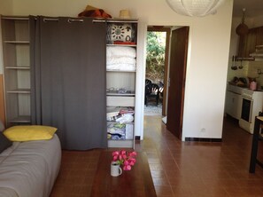 Quarto com cama, guarda-roupa, uma pequena mesa com flores e uma área de cozinha com fogão e armários.