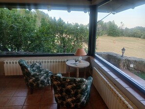A covered patio with two chairs, a table with a lamp, and a view of a field with trees. - Fantastic rural house "Amaltea" in Candeleda (Candeleda)