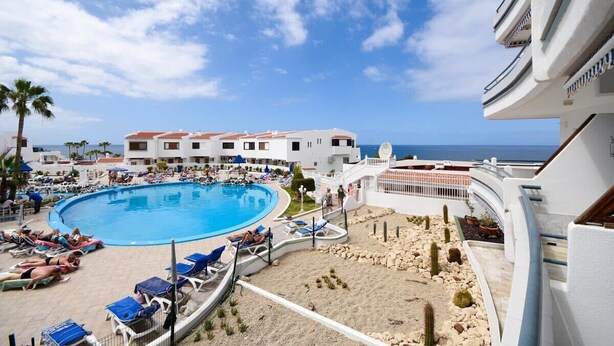 Ein Resort mit großem Pool, Liegestühlen und Blick aufs Meer.