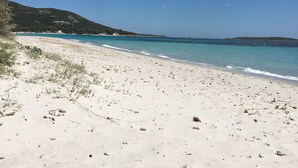 Une plage de sable blanc, une eau d’un bleu cristallin et un paysage vallonné en arrière-plan.