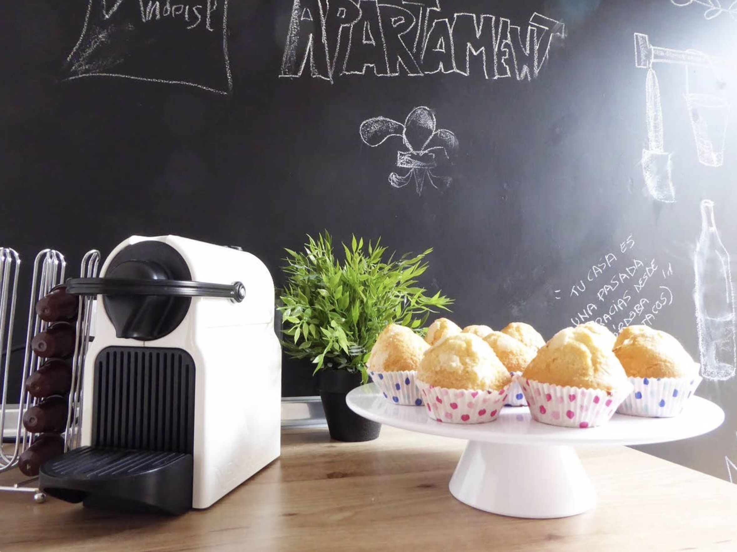 A kitchen counter with a coffee maker, a potted plant, and a stand holding cupcakes.