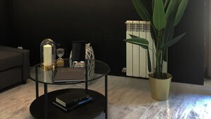 A modern living room with a black wall and a neon sign that reads "fuck media live real." There's a round glass coffee table with a book, a candle, and a glass. A large green plant is in a gold pot. - BEAUTIFUL DESIGN FLOOR IN THE CENTER OF AVILA FOR 6 PEOPLE (Ávila)