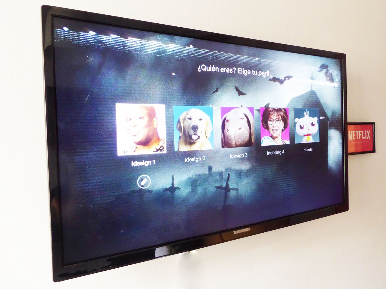 Een flatscreen televisie aan een muur, toont een interface voor profielkeuze.