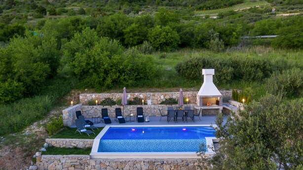 Zona junto a la piscina con paredes de piedra, sillones de descanso y un brasero.