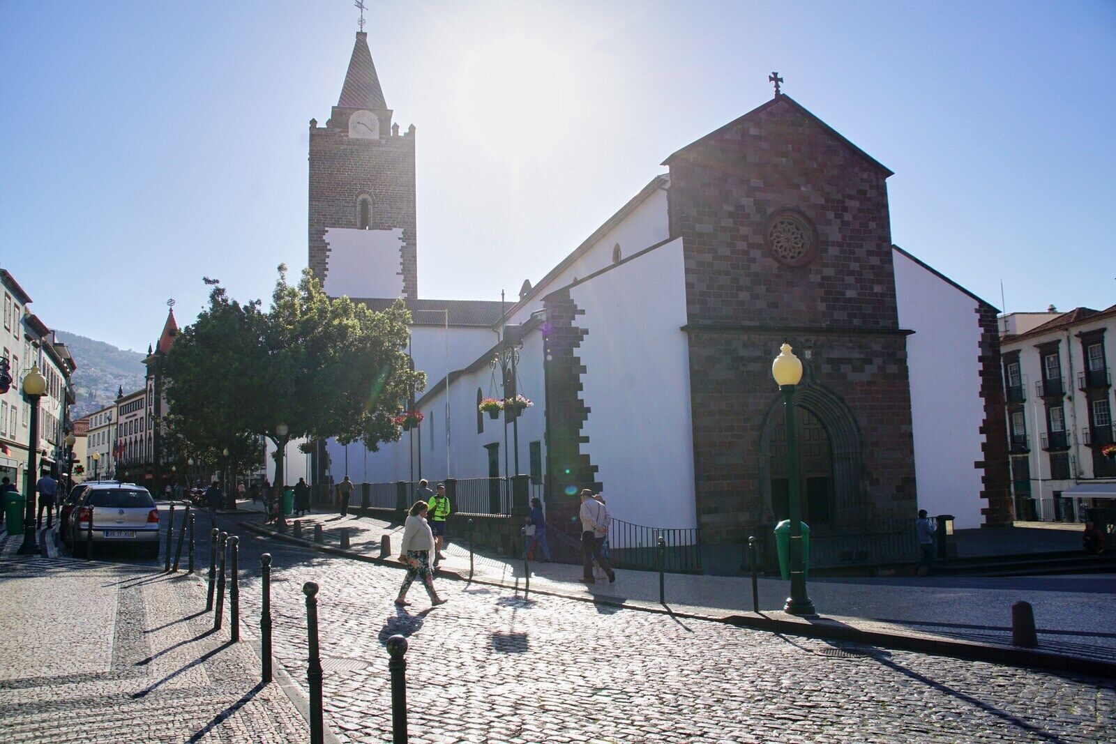 A cobblestone street with historic buildings, a church with a clock tower, and pedestrians.