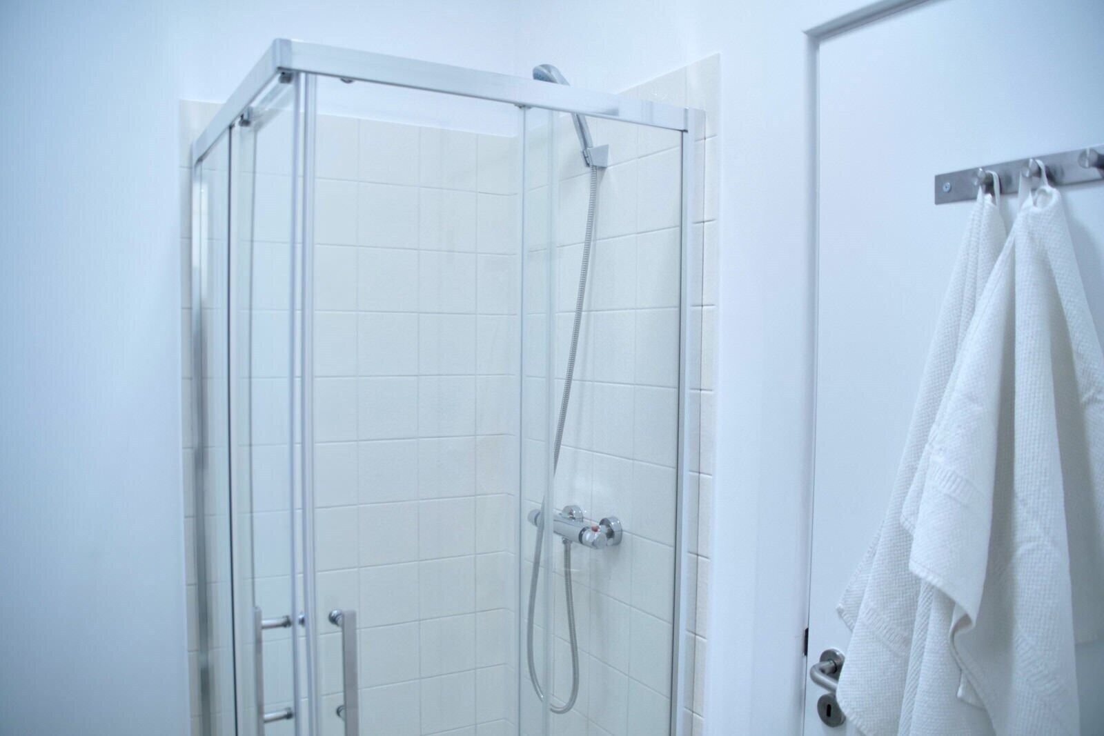 Une douche avec une porte en verre, un porte-serviettes avec des serviettes et un mur recouvert de carreaux blancs.