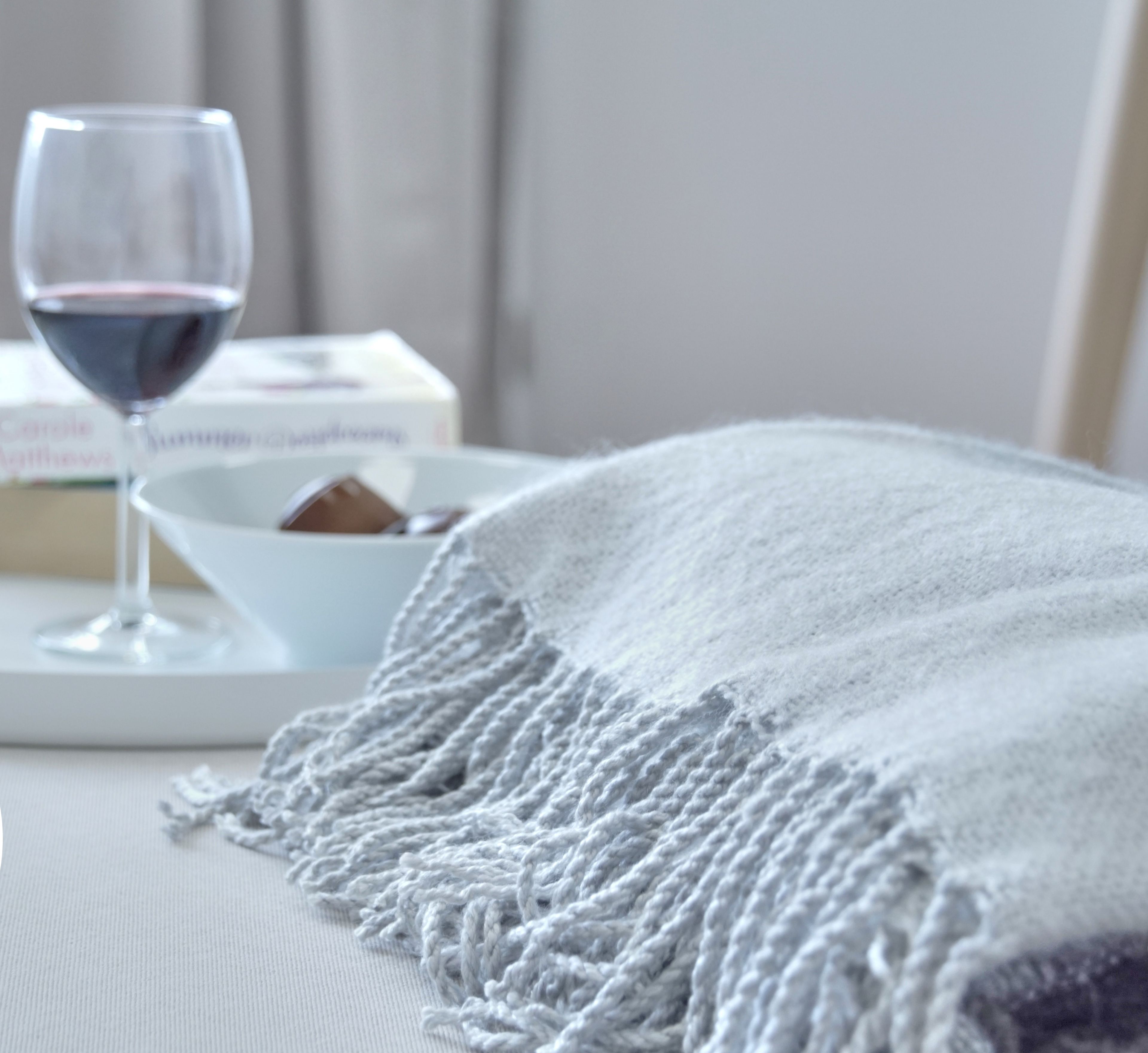 A cozy room with a white bed, a white blanket, and two glasses of red wine on a tray. There is a box of tissues and a small bowl on the bed.