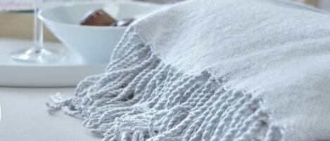 A cozy room with a white bed, a white blanket, and two glasses of red wine on a tray. There is a box of tissues and a small bowl on the bed.