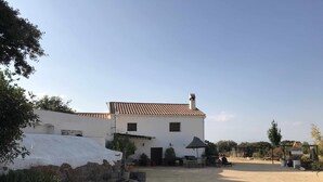 A white building with a tiled roof, a stone wall, and a gravel driveway. - Cortijo rural bacares 1 (Freila)