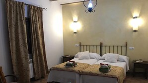 A double bed with a floral bedspread, two bedside tables, a nightstand, a glass coffee table, and a curtain with a floral pattern. - Cortijo rural bacares 1 (Freila)