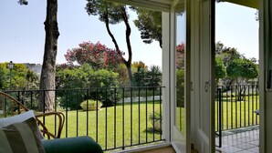 Un balcón con vistas a un césped cuidado y árboles, una silla y un farol.