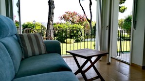 Una sala de estar con un sofá, una mesita y vistas a un jardín a través de un ventanal.